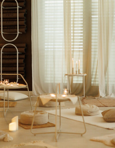 Ein ruhiger, gemütlicher Meditationsraum mit Bodenkissen, gewebten Matten und kleinen Tischen mit Kerzen - perfekt für Coaching, Pilates und Yoga in Bruchsal. Gerollte Matten und minimalistisches Dekor tragen zu einer ruhigen Atmosphäre bei, die von sanftem Tageslicht begleitet wird.