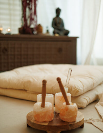 Ein ruhiges Spa-Ambiente für Pilates und Yoga in Bruchsal, mit Salzkerzenhaltern, Holzstäben und Glasstäben auf einem Tablett, dazu gefaltete weiße Kissen und eine Buddha-Statue - perfekt zum Entspannen oder achtsamen Coaching.